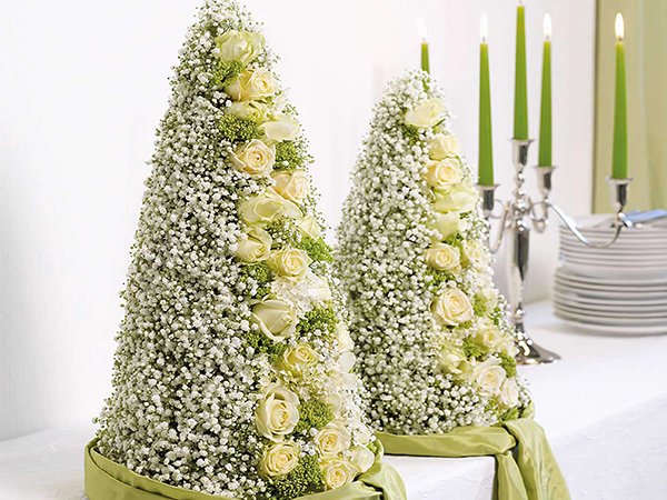 Two cone-shaped floral arrangements with white roses and baby's breath, on a table with candles and plates.