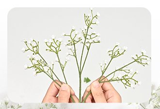 Hands arranging stems of white artificial baby's breath flowers against a white background.