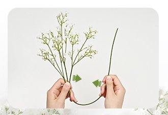 Hands bending a stem of white artificial baby's breath flowers against a white background.
