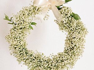 White artificial baby's breath wreath with a cream ribbon bow and green leaves