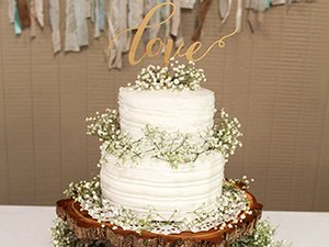 Two-tier white cake decorated with baby's breath flowers and a wooden 'love' cake topper.