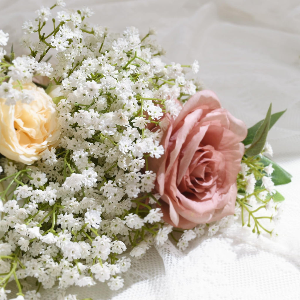 Bouquet of artificial baby's breath with a pink rose and a cream rose, on a white lace background.