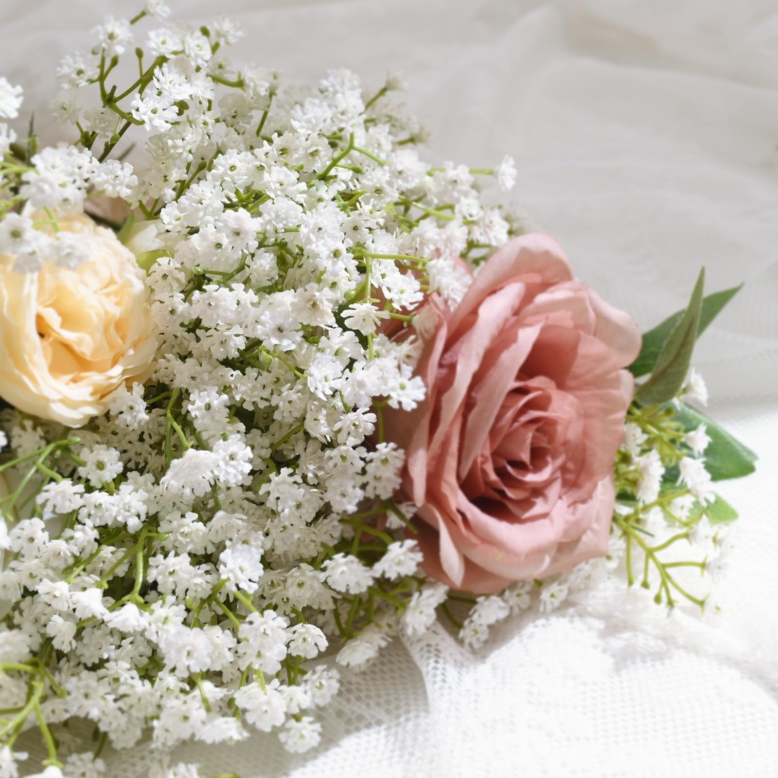 Bouquet of artificial baby's breath with a pink rose and a cream rose, on a white lace background.