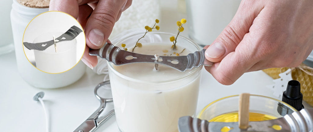Hands using a metal wick centering tool on a candle, with a close-up inset showing the tool on another candle.