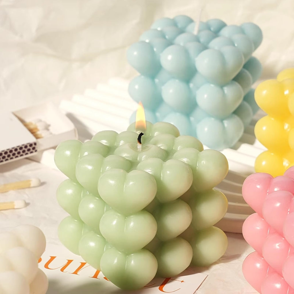 Close-up of a lit green heart-shaped bubble candle with other colored candles in the background and matches on the side.