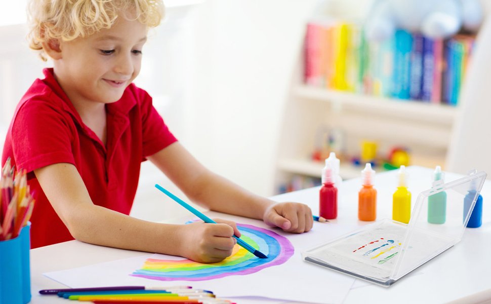 Young boy in red shirt painting a rainbow with a blue brush at a table with art supplies and a wet palette kit.