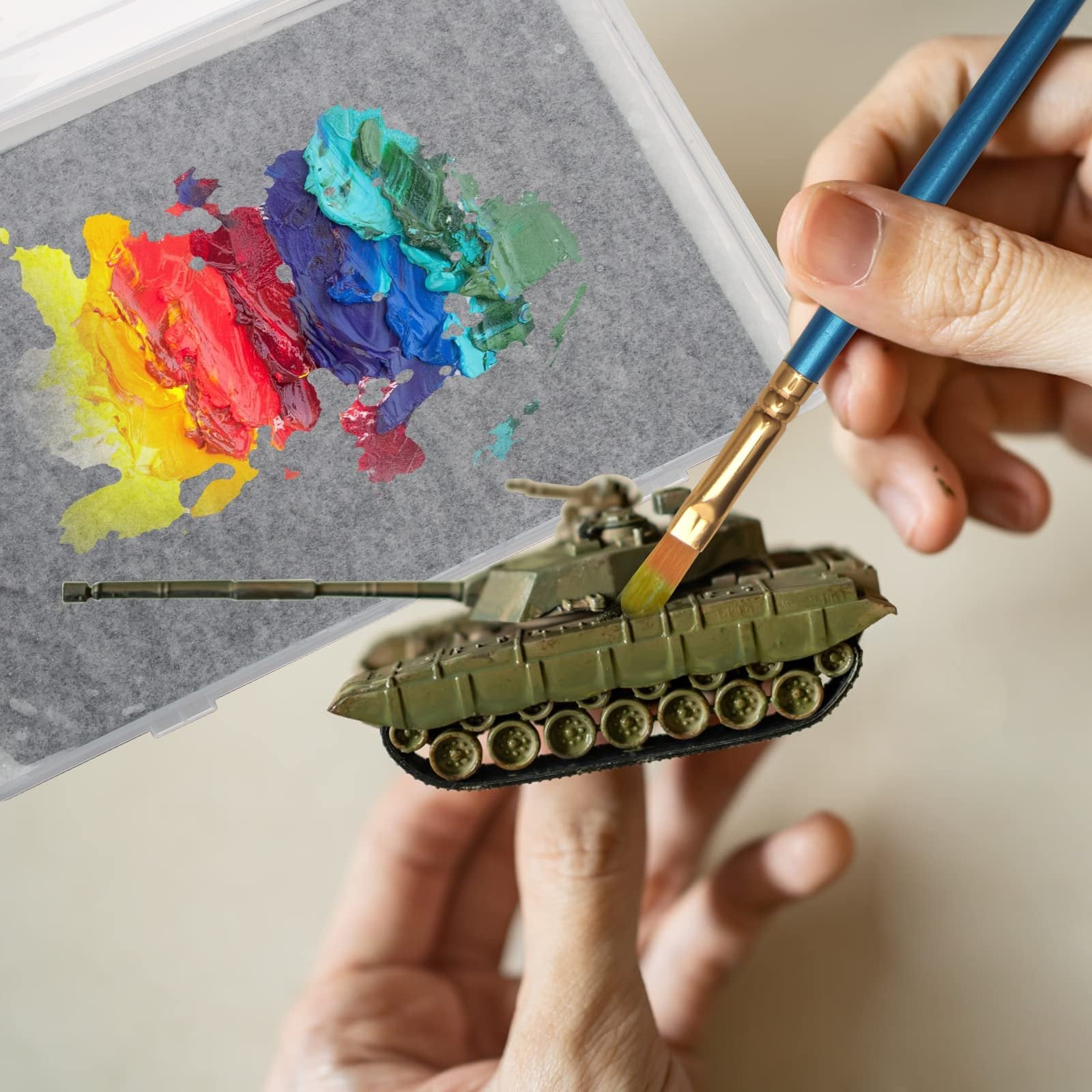 Hands painting a model tank with a brush dipped in colorful paints on a wet palette