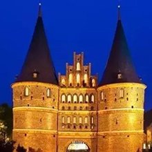 Historic Holsten Gate in Lubeck, Germany at dusk with illuminated brickwork and dark blue sky