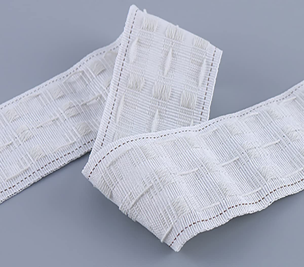 White curtain pleating tape with a textured grid pattern and stitched edges, shown on a gray background.
