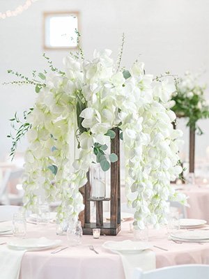 White wisteria garland cascading from a wooden lantern centerpiece on a pink tablecloth