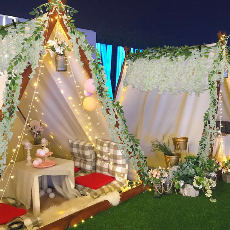 White wisteria garlands draped over a tent structure with fairy lights and cushions inside.