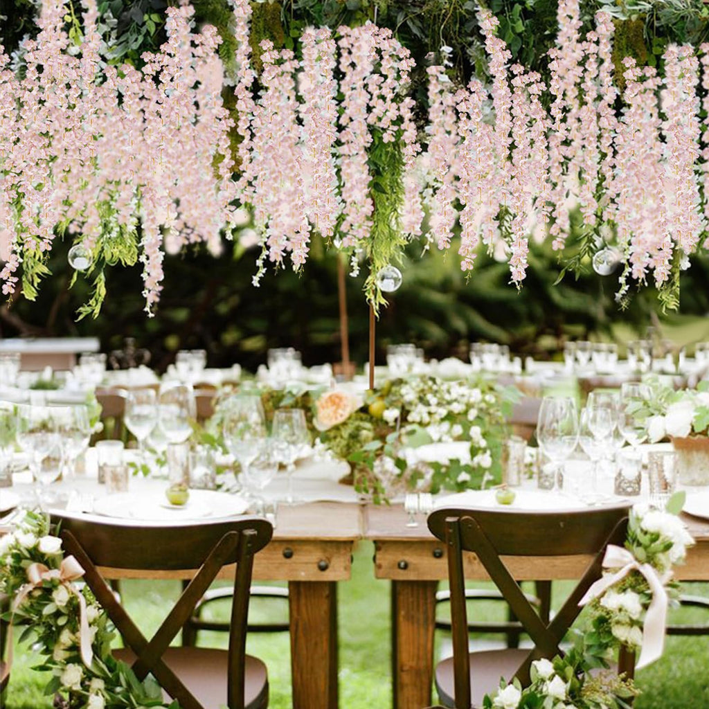 Wedding reception tables decorated with pink wisteria garlands and floral arrangements, set outdoors.