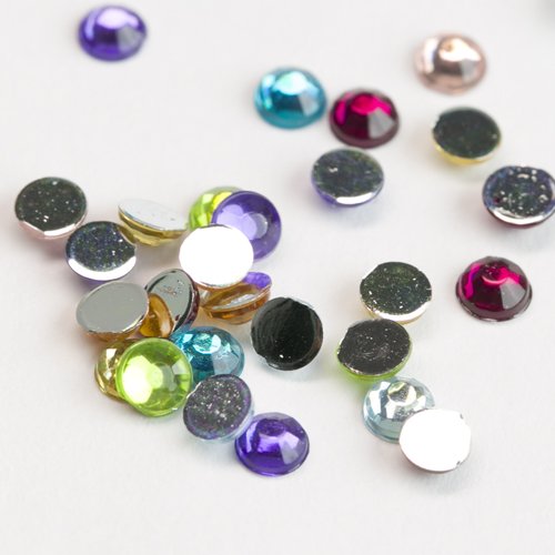 Scattered round flatback rhinestones in various colors including purple, teal, pink, yellow, and clear on a white background.