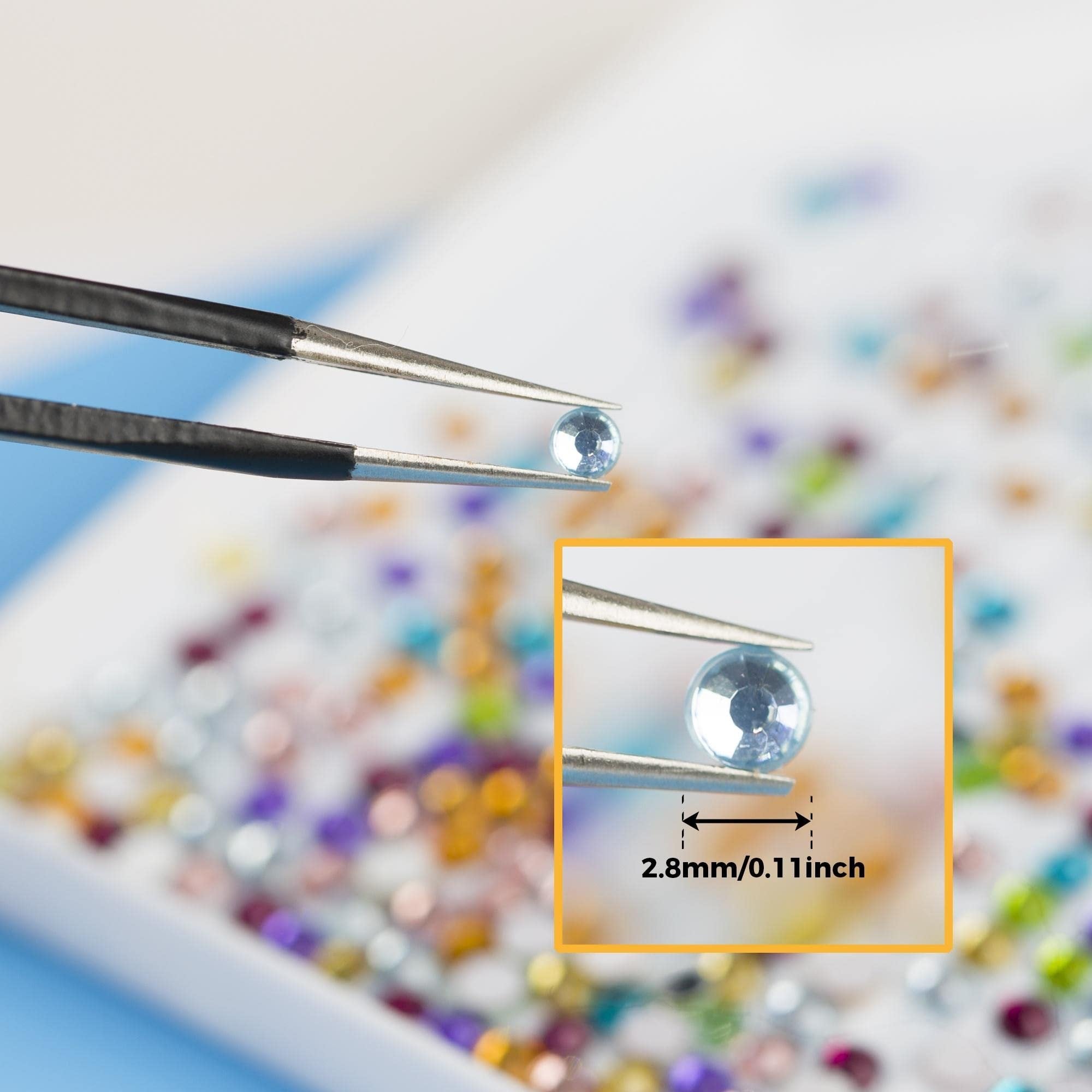 Close-up of tweezers holding a single round flatback rhinestone, with an inset showing its size as 2.8mm/0.11inch. The background is a tray filled with colorful rhinestones.