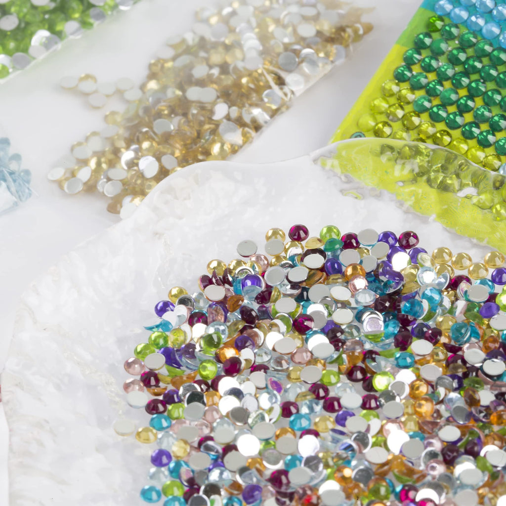 Assorted colorful round flatback rhinestones for diamond painting, scattered on a white surface and in plastic bags.