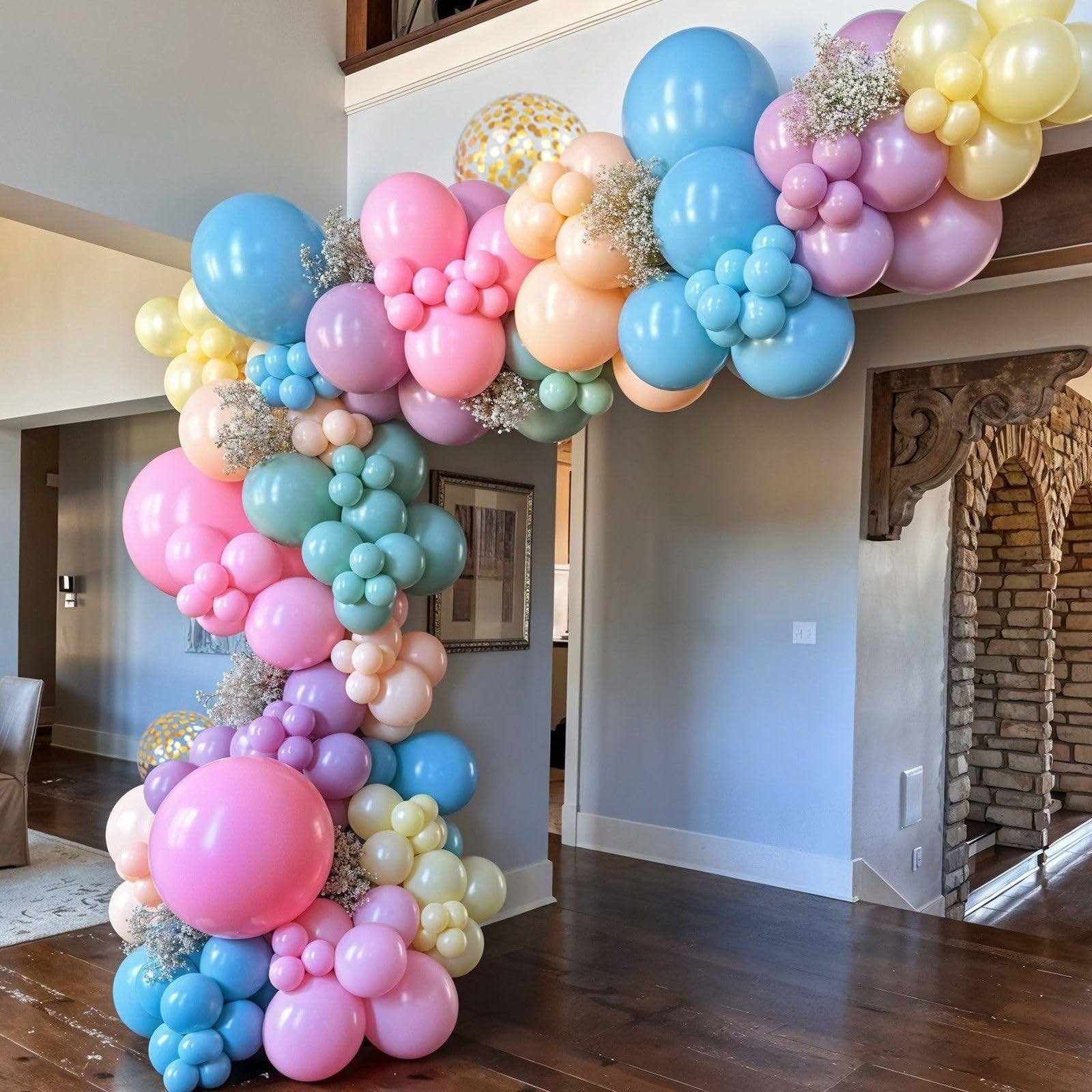 Pastel balloon arch with gold confetti balloons and white filler flowers in a home entryway.
