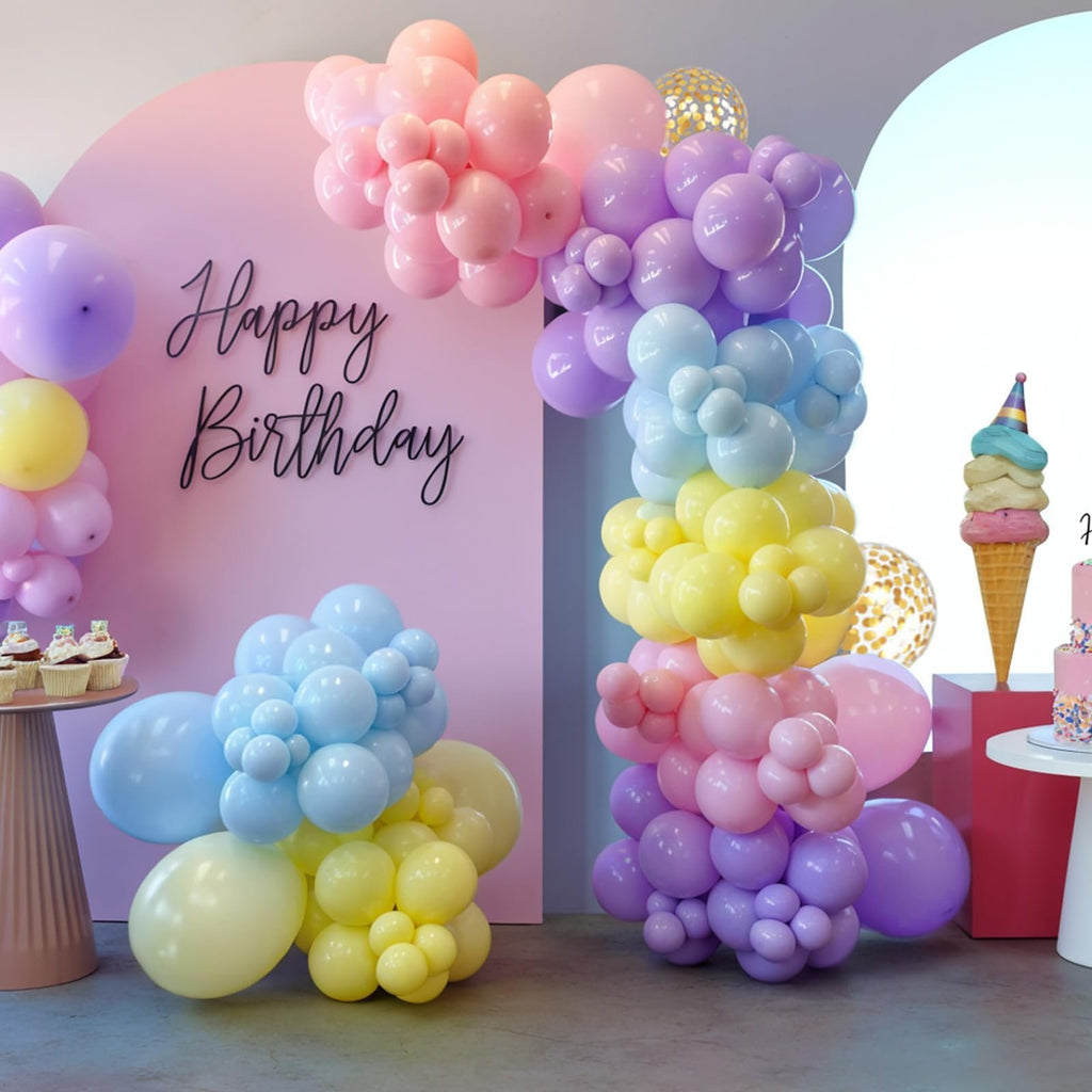 Pastel balloon garland arch and clusters in pink, purple, yellow, and blue, with 'Happy Birthday' text on a pink backdrop.