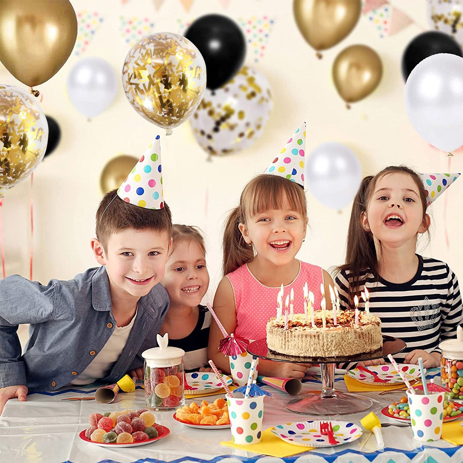 Children celebrating a birthday with a cake and balloons, featuring black, gold, and white balloons with confetti.