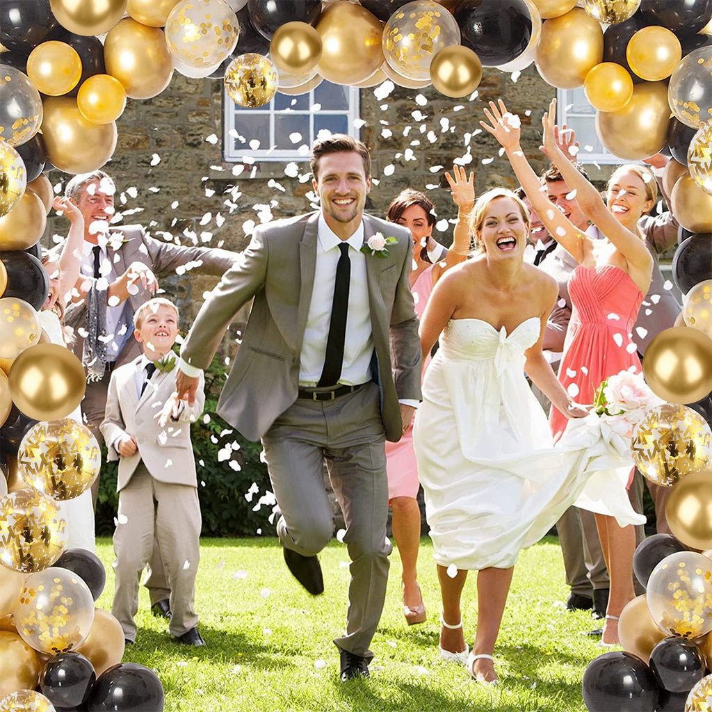 Wedding party running through confetti with black, gold, and confetti balloons overhead