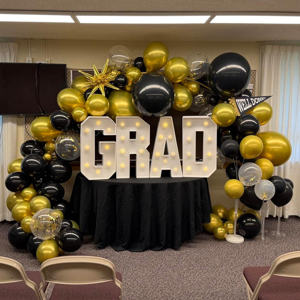 Graduation party balloon arch and marquee letters spelling GRAD, with a black tablecloth and chairs in foreground.