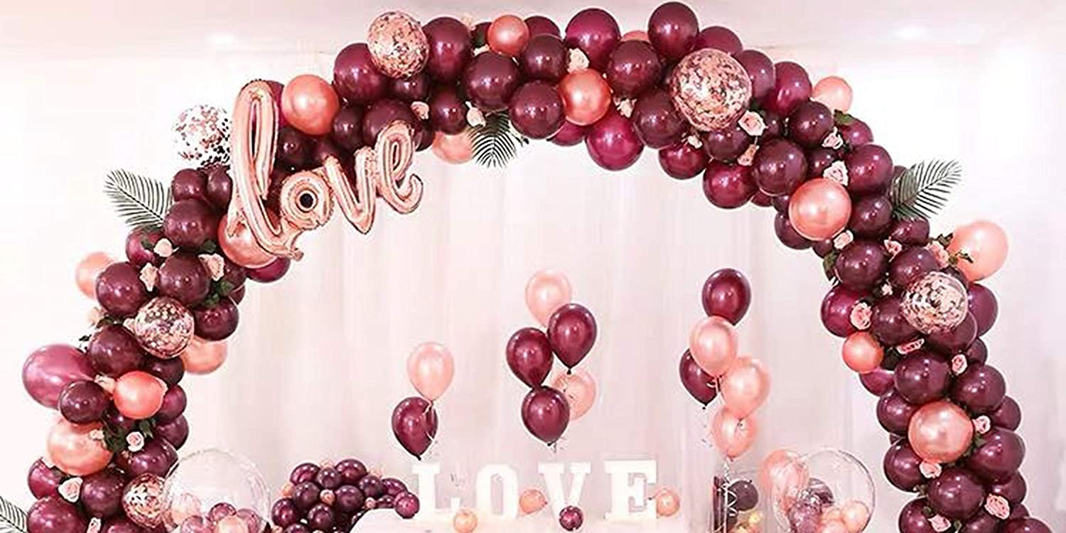 Balloon arch in burgundy, rose gold, and confetti with a rose gold 'love' balloon decoration.