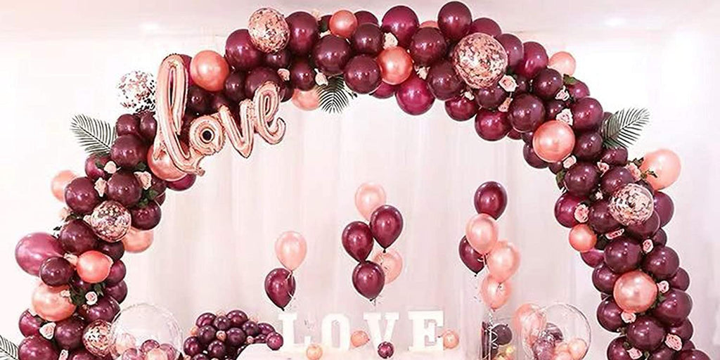 Balloon arch in burgundy, rose gold, and confetti with a rose gold 'love' balloon and white 'love' letters below.