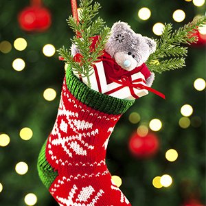 Christmas stocking filled with a teddy bear, gift box, and pine sprigs against a bokeh background of Christmas lights.
