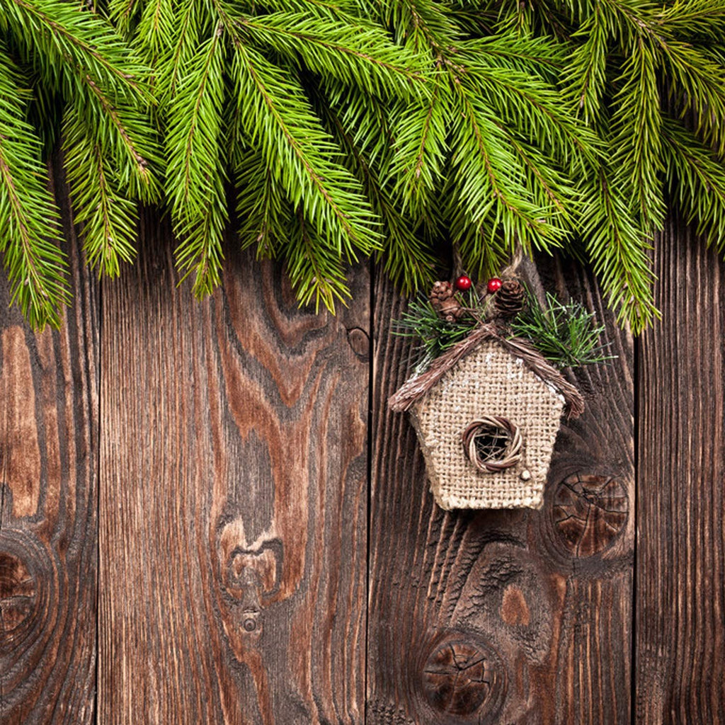 Christmas decoration of a small burlap house with pine sprigs and berries on a rustic wooden background with pine branches overhead
