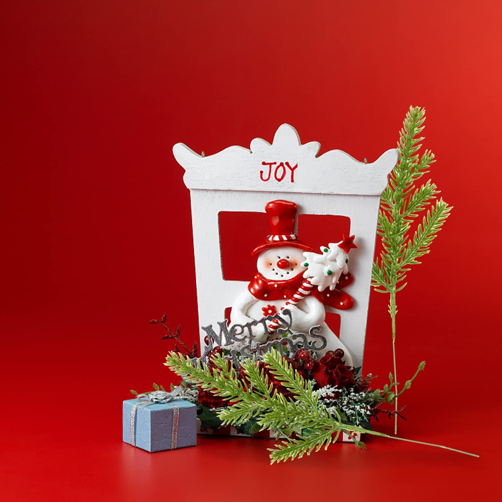Christmas snowman decoration with 'Joy' and 'Merry Christmas' text, holding a small tree, with a gift box and pine sprigs.