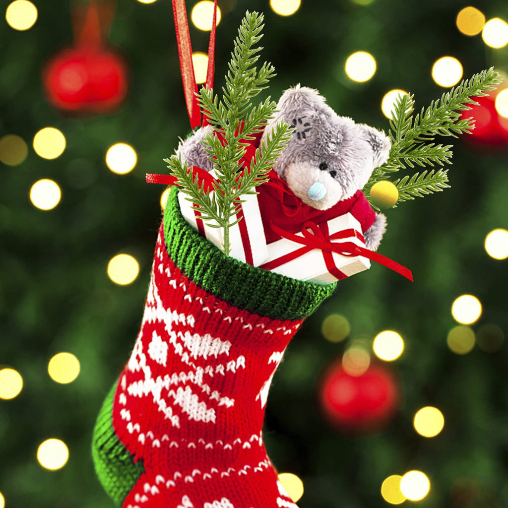 Christmas stocking filled with a teddy bear, gift, and pine sprigs against a blurred Christmas tree background.