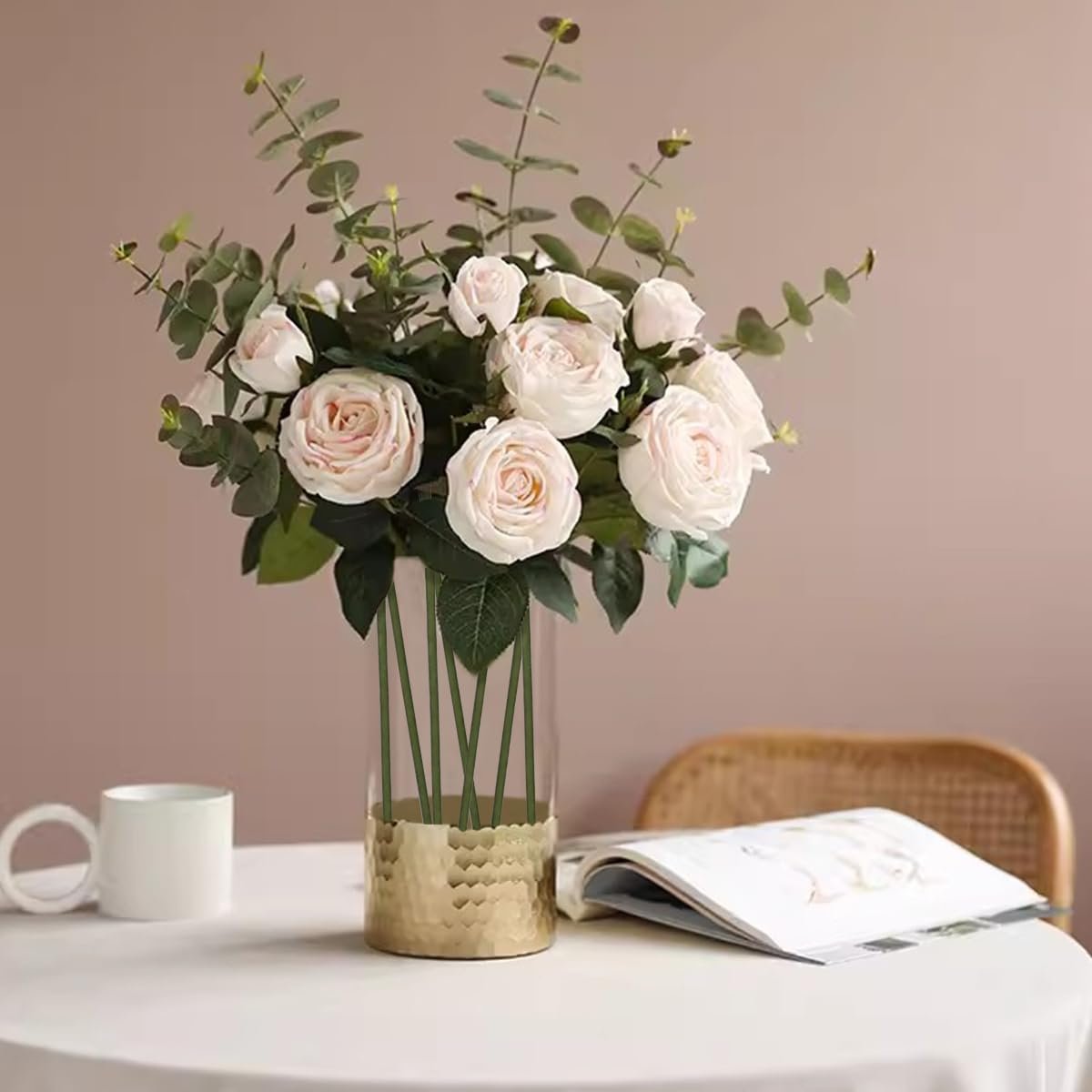 Vase of light pink roses and eucalyptus with green floral wire stems on a table with a mug and book