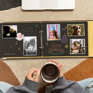 Open scrapbook photo album with black pages, featuring photos of couples and dogs, decorated with birthday graphics and text.