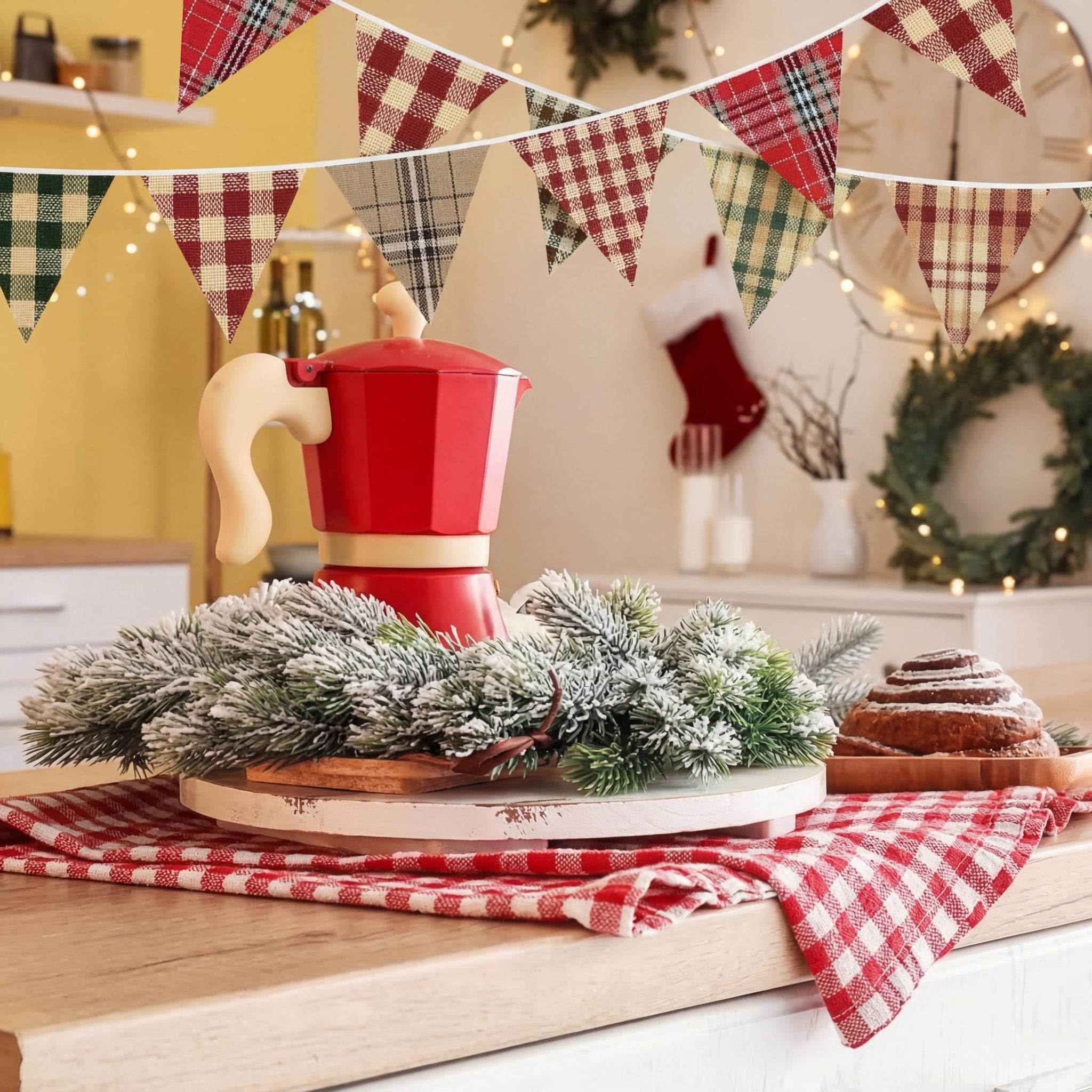 Christmas kitchen scene with plaid bunting, red coffee maker, frosted pine branches, and a cinnamon roll
