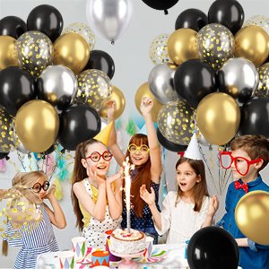 Children celebrating a birthday party with black, gold, and silver balloons and a cake.