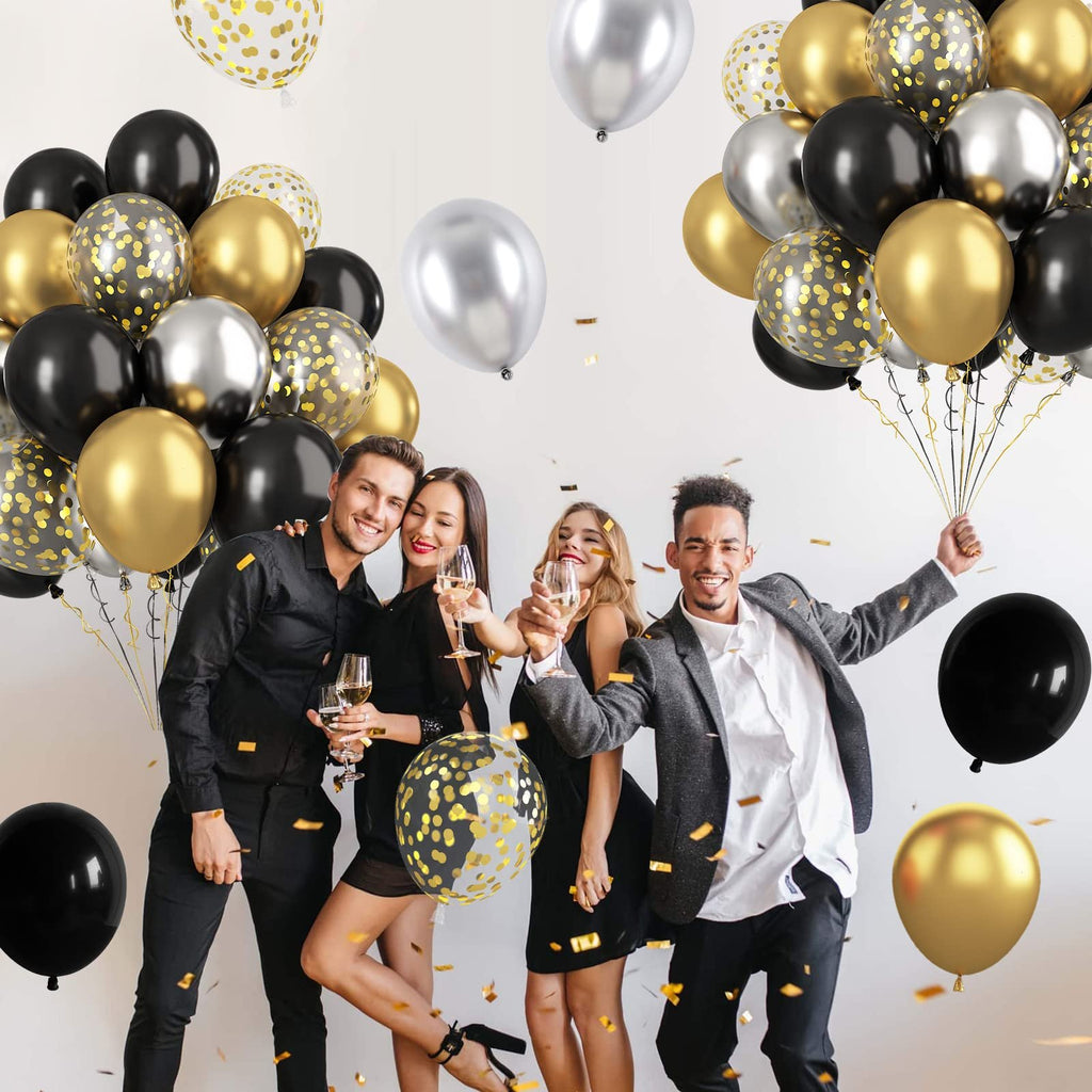 Four people celebrating with black, gold, and silver balloons and confetti