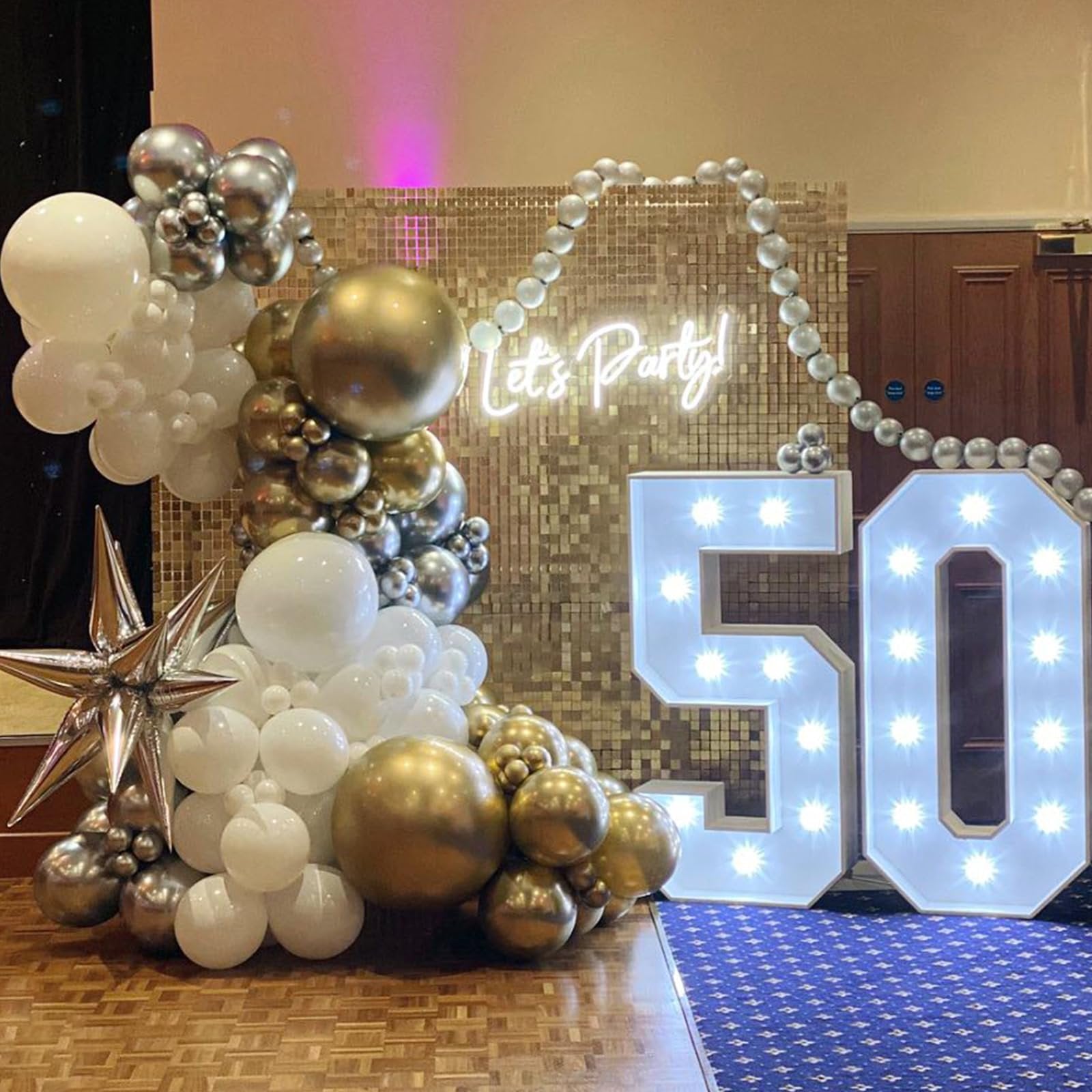 Balloon arch with gold, silver, and white balloons, a starburst balloon, and light-up '50' numbers for a party.