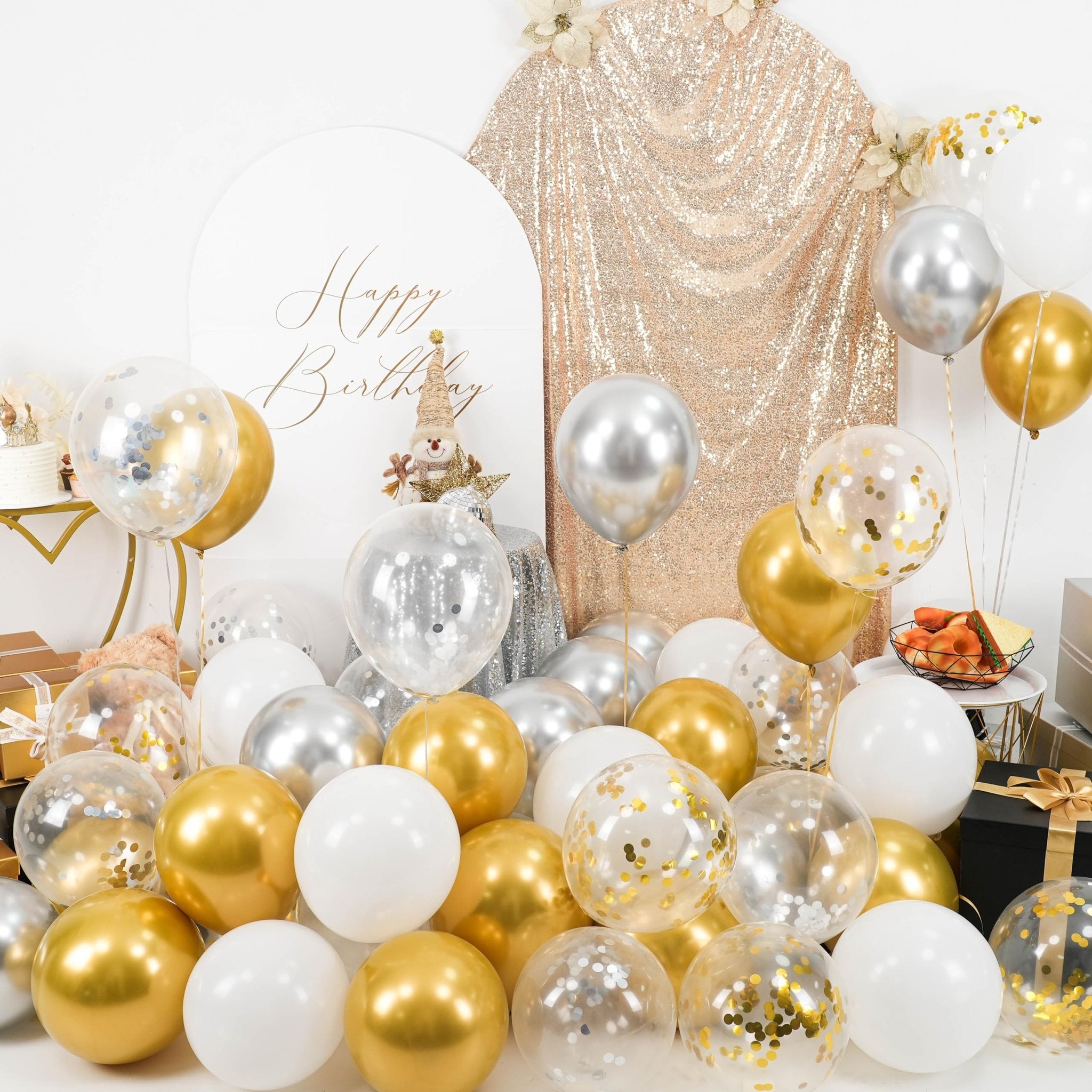 Assortment of metallic gold, silver, and white balloons, some filled with confetti, arranged for a party setting.