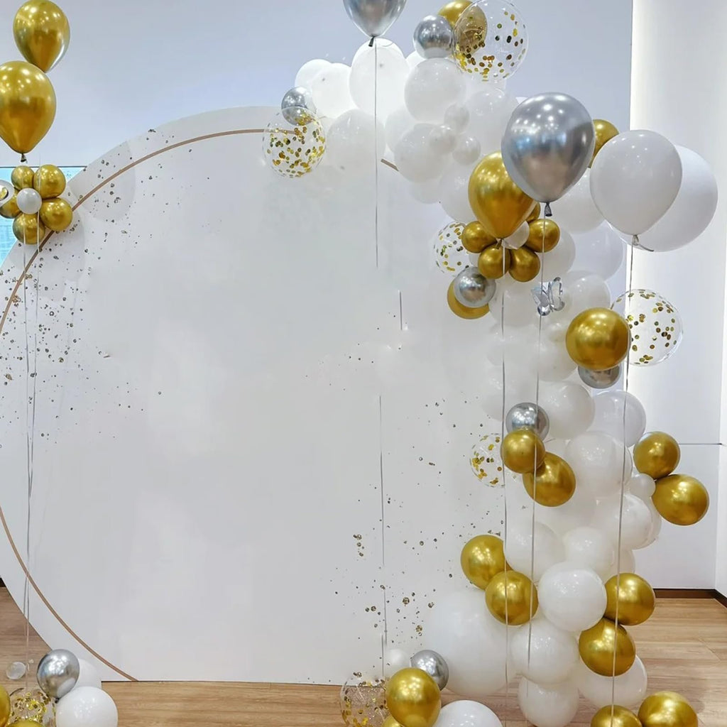 Gold, silver, and white balloons arranged in an arch around a circular backdrop for a party or event.