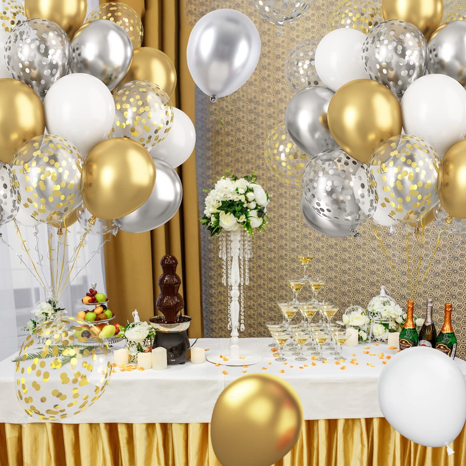Metallic gold, silver, and white confetti balloons arranged for a party setting with a chocolate fountain and champagne tower.