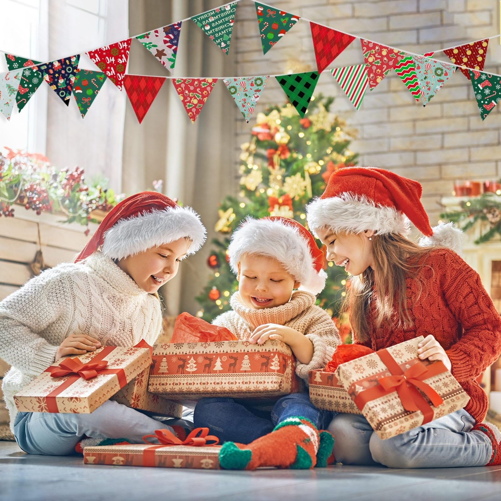 Three children in Santa hats opening Christmas gifts with a decorated tree in the background and festive bunting overhead.