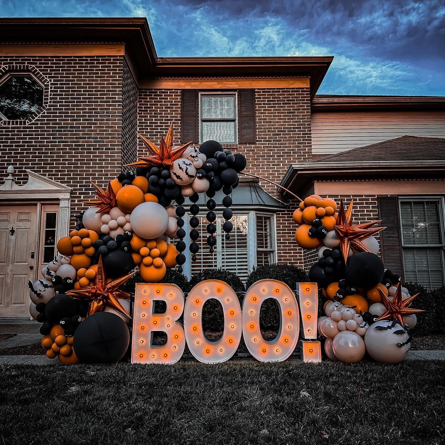 Halloween balloon arch and light-up 'BOO!' sign in front of a brick house