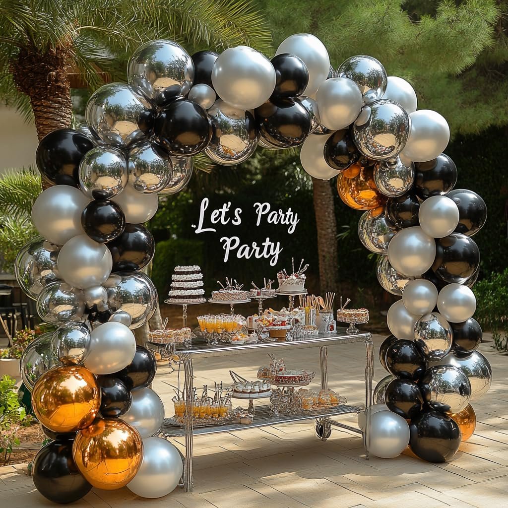 Black, white, silver, and gold balloons arching over a dessert table with cakes and drinks.