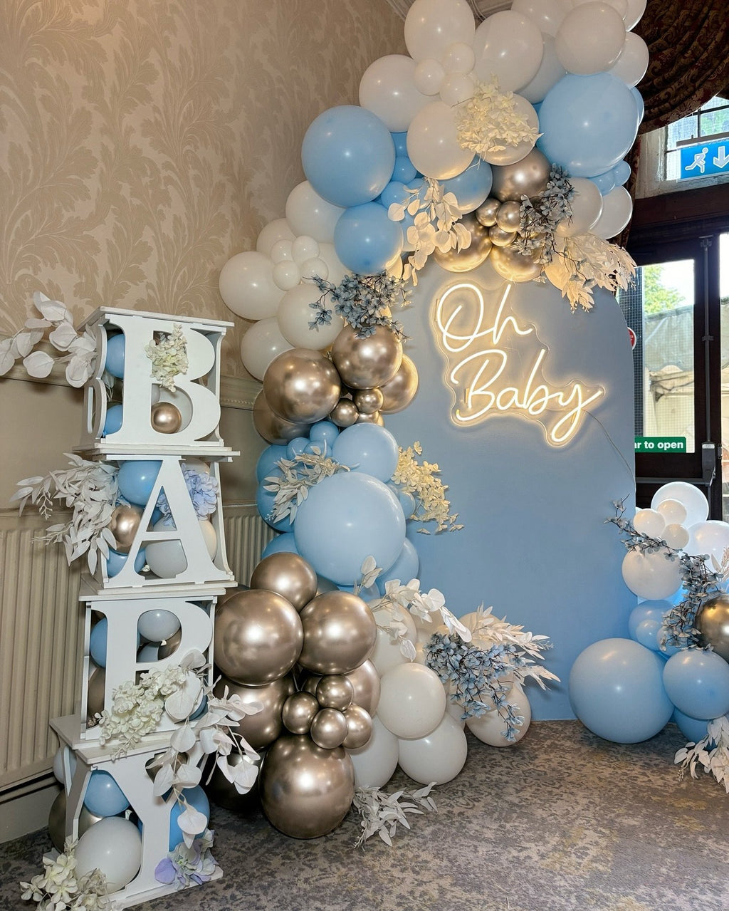 Dusty blue, white, and champagne gold balloon arch with 'Oh Baby' neon sign and white decorative letters spelling 'BABY'.