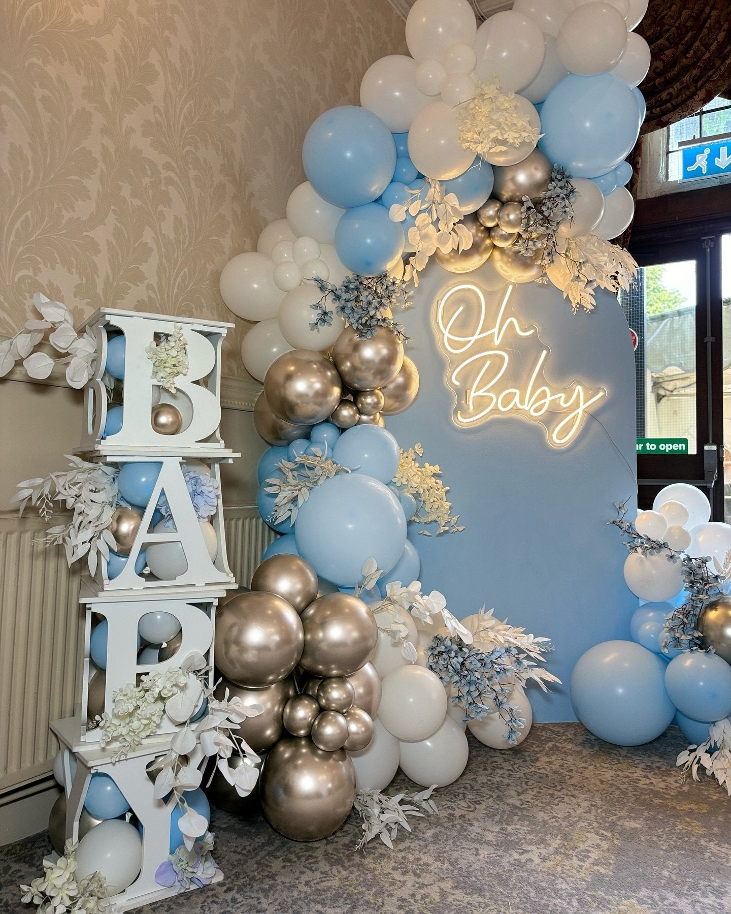 Dusty blue, white, and champagne gold balloon arch with 'Oh Baby' neon sign and white decorative letters spelling 'BABY'.