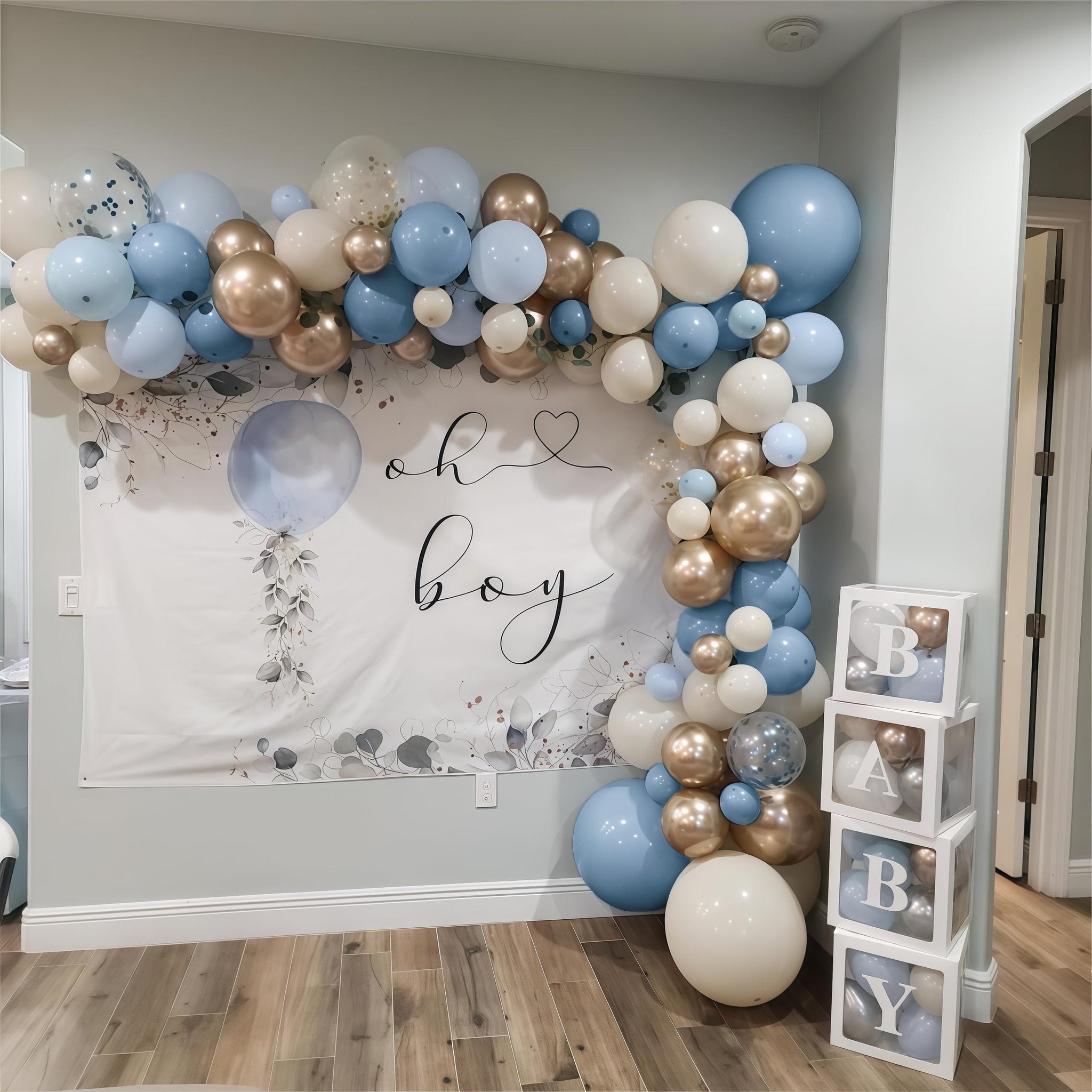 Dusty blue, champagne gold, and white balloons arranged in an arch and cluster around a 'oh boy' banner and decorative blocks.