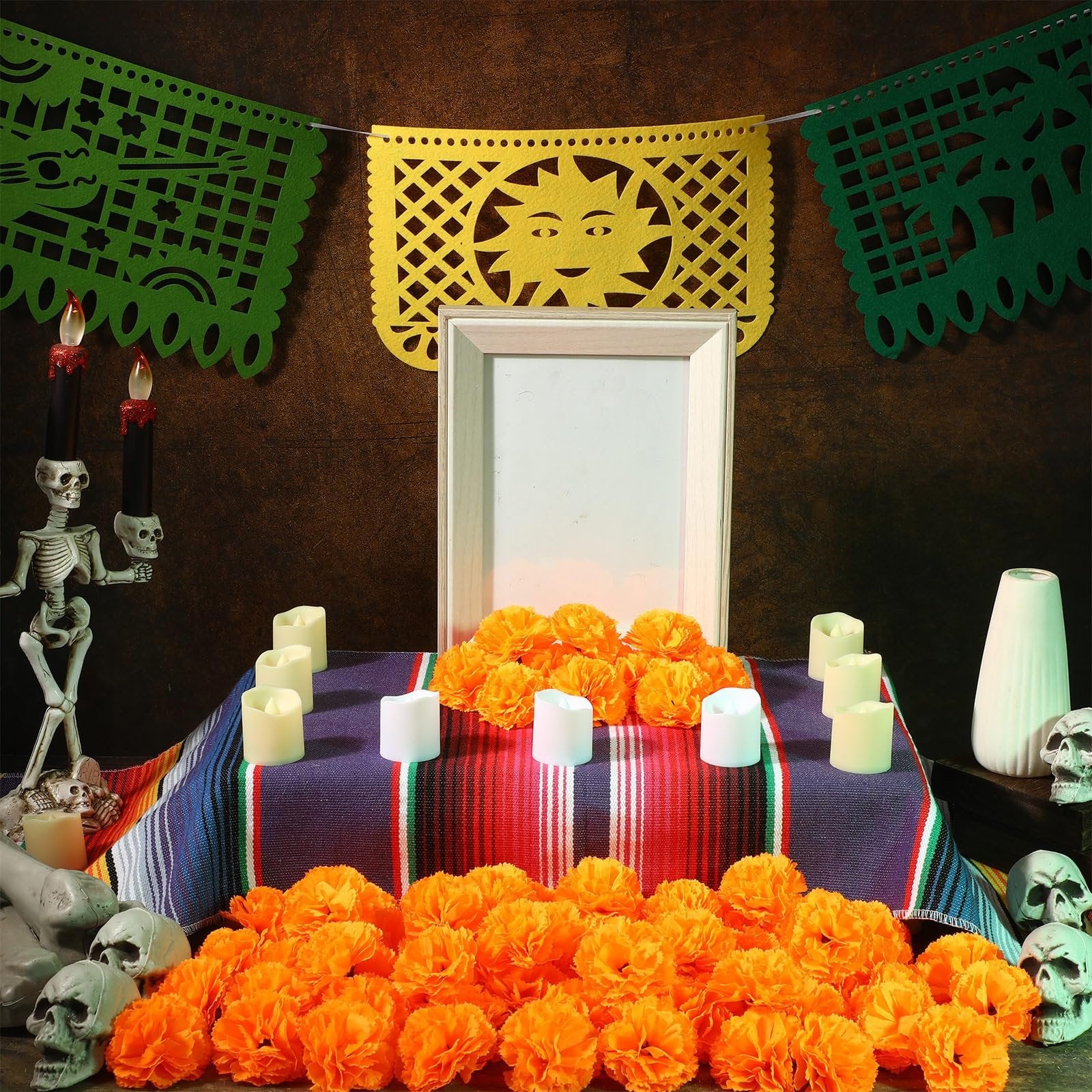 Day of the Dead altar setup with marigold flowers, papel picado banners, candles, and a photo frame.