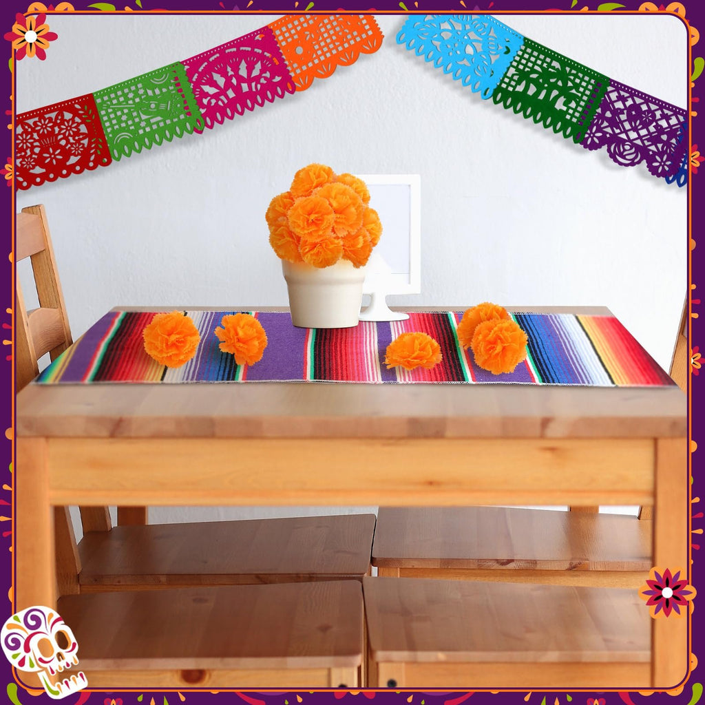 Day of the Dead table setting with papel picado banners, marigold flowers, and a striped table runner on a wooden table.