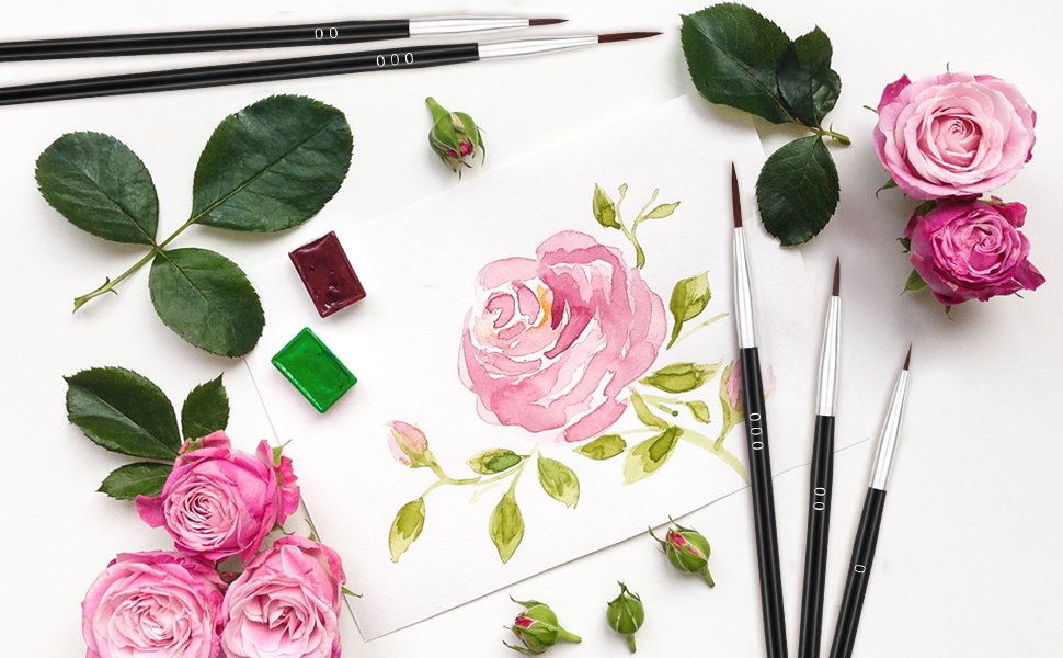 Fine tip paint brushes arranged with a watercolor painting of a rose, paint pans, and rose blooms on a white surface.