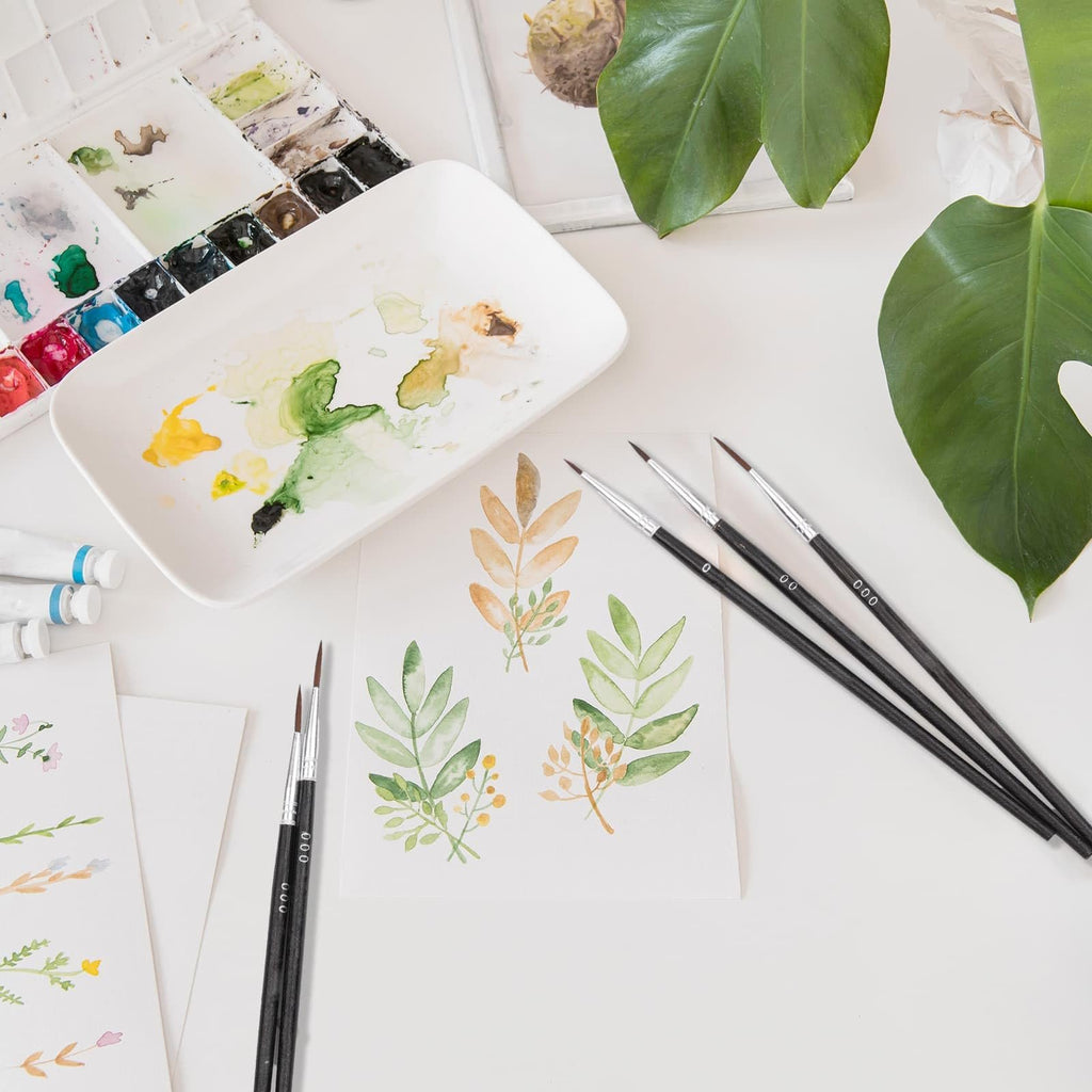 Watercolor painting supplies including brushes, paint palette, and painted leaves on paper.