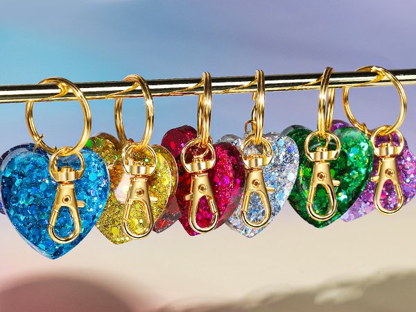Assortment of glitter heart-shaped charms with gold swivel snap hooks and key rings hanging on a gold bar.